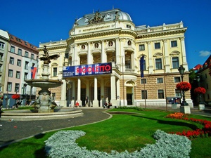 Pohľad na fasádu historickej budovy Slovenského národného divadla z Hviezdoslavovho námestia v Bratislave so zakvitnutými záhonmi v popredí.